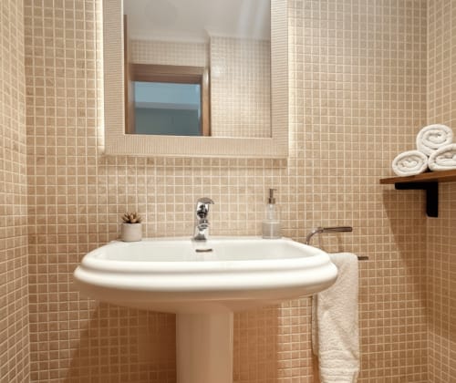 Baño moderno en tonos beige con lavabo pedestal, espejo grande y toallas enrolladas en estantería del apartamento Arco Da Vella de Holibai