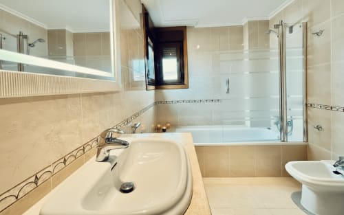 Baño moderno con azulejos beige, lavabo, bañera, ducha e inodoro en el apartamento Arco Da Vella de Baiona