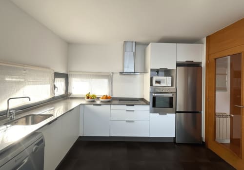 Moderna cocina del apartamento dúplex Beiramar en Baiona con muebles blancos, electrodomésticos de acero inoxidable y vistas al mar