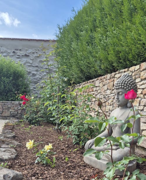 Boeddhabeeld met roze bloem in de tuin van Moulin Renaudiots te Autun, omgeven door groen en stenen muren
