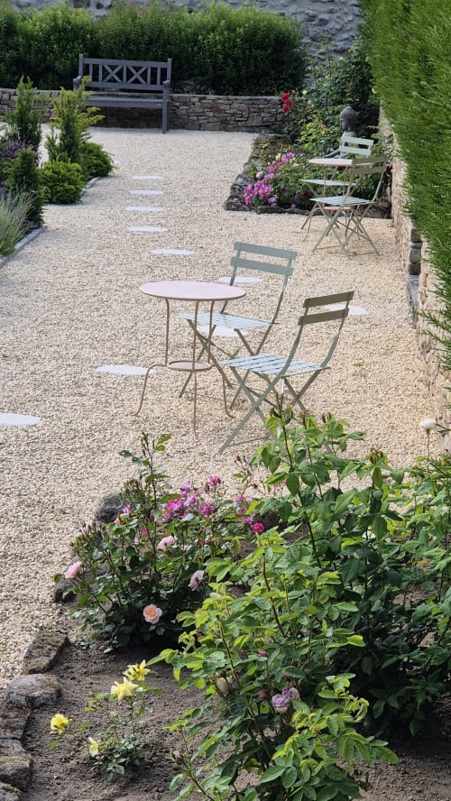Rustig tuinzitgedeelte bij hotel Moulin Renaudiots in Autun met kiezelpadjes, bloeiende rozen en bistrostoelen