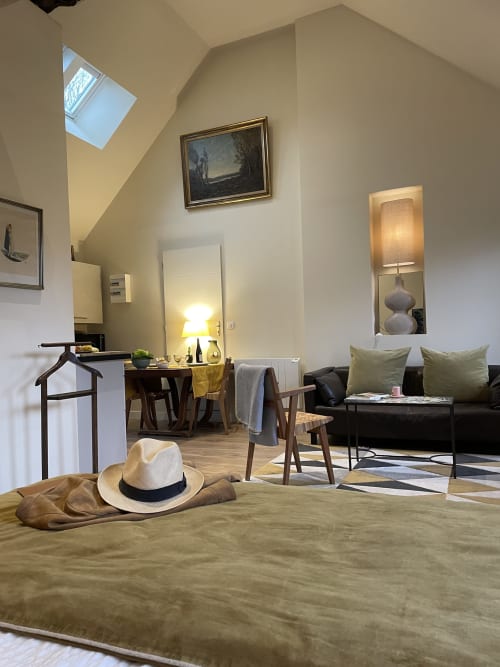 Clairseine B&B studio in Tournedos-sur-Seine with cream walls, skylight, black sofa, wooden furniture and hat on bed