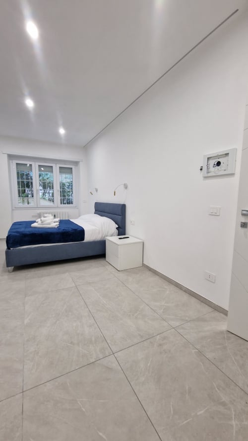 Camera moderna a Zoelia Roma con letto blu, pareti bianche, pavimento in marmo, finestre con vista sulla città e termostato intelligente