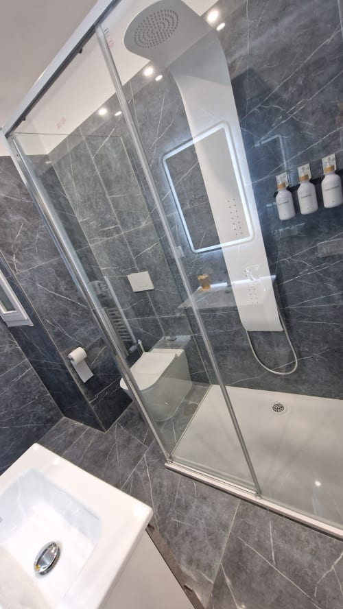 Bagno moderno dell'appartamento Zoelia Cipro a Roma, con piastrelle in marmo scuro, cabina doccia in vetro, sanitari bianchi