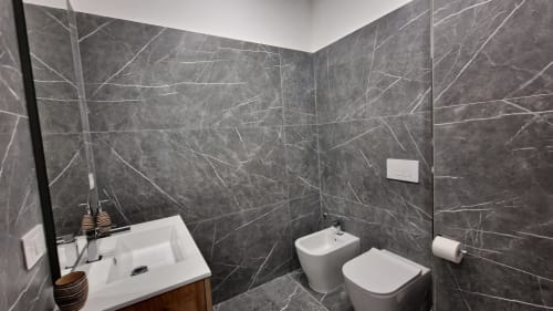 Bagno moderno a Zoelia Roma con piastrelle in marmo scuro, lavabo bianco, bidet, toilette e portarotolo