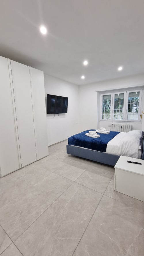 Camera da letto moderna dell'appartamento Zoelia Roma con letto blu, armadio bianco, TV a parete e vista sulla città