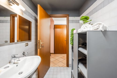 Bagno moderno con piastrelle bianche, porte in legno, lavabo e ripostiglio presso Le Arche hotel apartment a Verona