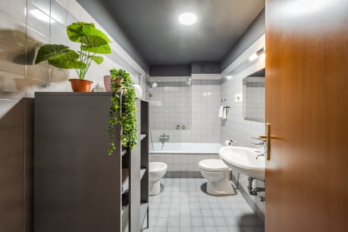 Bagno moderno dell'appartamento Le Arche a Verona con piastrelle bianche, doppio lavabo, vasca e piante verdi