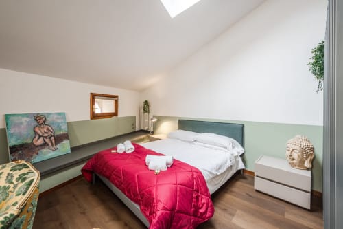 Camera moderna dell'appartamento Le Arche Verona con testata verde, biancheria rossa, lucernario e arredamento contemporaneo