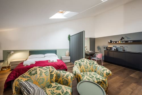 Moderno appartamento Le Arche a Verona con letto matrimoniale, poltrone decorate, lucernario e angolo cottura sotto soffitto spiovente.