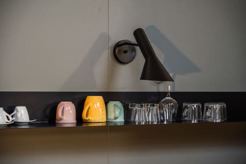 Moderna mensola nella camera dell'hotel Le Arche a Verona con tazze di ceramica colorata, bicchieri e lampada a sospensione nera