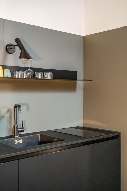 Angolo cucina moderno nell'appartamento Le Arche di Verona, con piano di lavoro nero, lampada a parete e mensola in legno