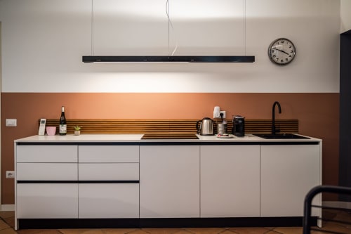 Angolo cottura moderno nell'appartamento Le Arche di Verona con mobili bianchi, parete in terracotta e elettrodomestici in acciaio inox