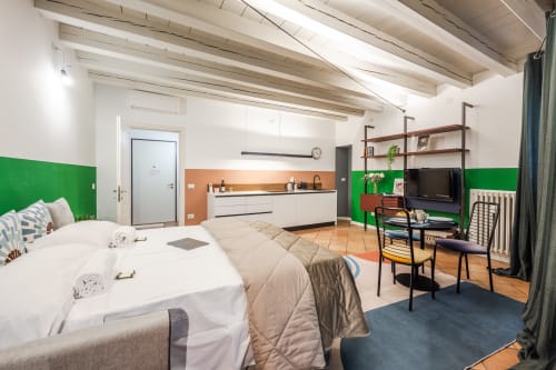 Moderno monolocale a Verona con letto, angolo cottura, TV, parete verde salvia e soffitto con travi in legno