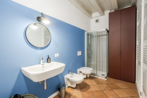 Bagno moderno dell'appartamento Le Arche a Verona con pareti blu, specchio rotondo, lavabo, wc, bidet e doccia