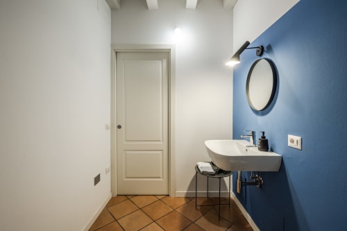Bagno moderno nell'appartamento Flumen presso Le Arche, Verona, con parete azzurra, specchio rotondo e lavabo a bacinella