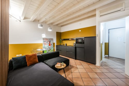 Moderno appartamento a Le Arche Verona con divano nero, parete gialla, cucina a vista e pavimento in cotto