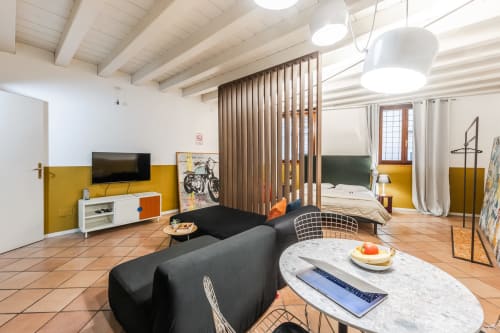 Moderno appartamento a Verona con divano nero, parete accent gialla, divisorio in legno e zona notte arredata con vista sulla città