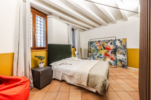 Camera da letto moderna all'Le Arche Verona con pareti gialle, travi a vista, pavimento in cotto e finestra con vista sulla città