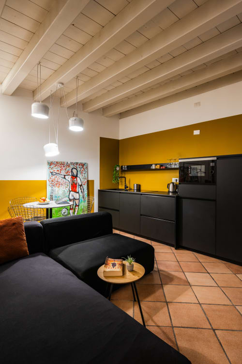 Appartamento Le Arche a Verona con divano nero moderno, parete gialla, cucina e travi in legno a vista