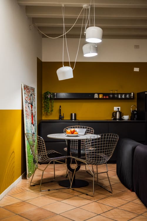 Zona cucina-pranzo moderna dell'appartamento Le Arche Verona con parete gialla, lampadari a sospensione e sedie metalliche geometriche