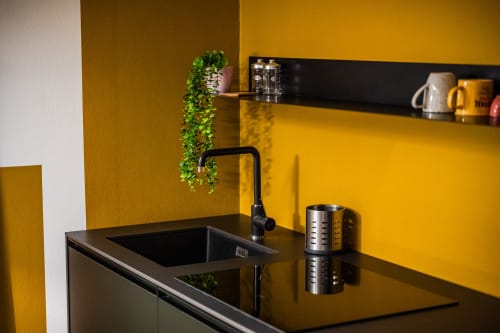 Lavello moderno con rubinetto nero nell'appartamento Le Arche di Verona, con pareti gialle e pianta verde decorativa sospesa