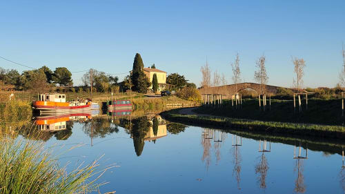 Barques orange amarrées sur l'eau calme de la villa Le N°9 à Argeliers, France, avec reflets de villa jaune et de bouleaux
