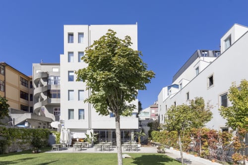 Benefit Collection hotel courtyard in Porto with modern white buildings, green lawn, outdoor seating, and tall tree under