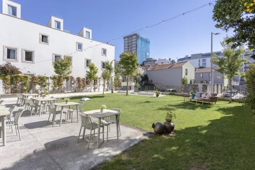 Modern hotel courtyard in Porto with green lawn, dining tables, white building facade, and city skyline views under clear