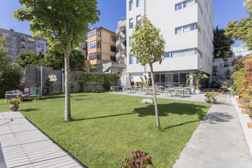 Sunny courtyard at Benefit Collection hotel in Porto with green lawn, modern white building, and outdoor dining area