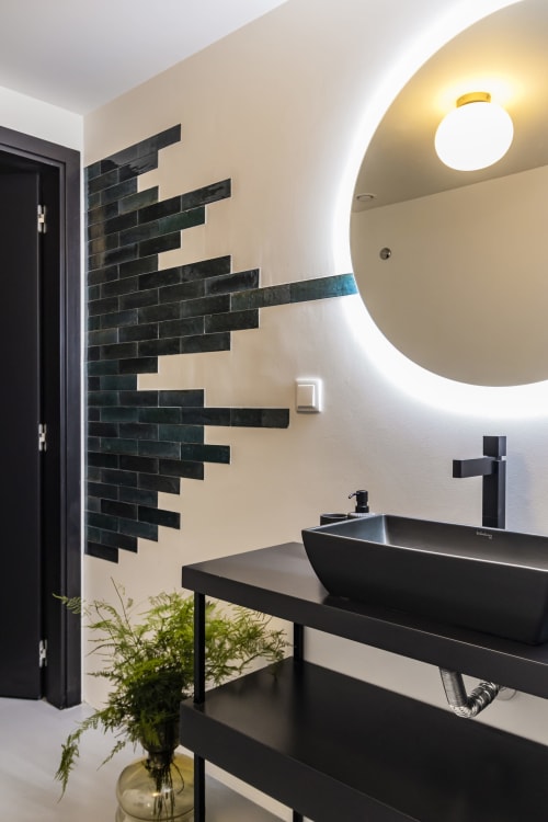 Baño moderno en estudio de hotel en Porto con lavamanos negro, espejo circular iluminado, pared de acento con azulejos negros y verde