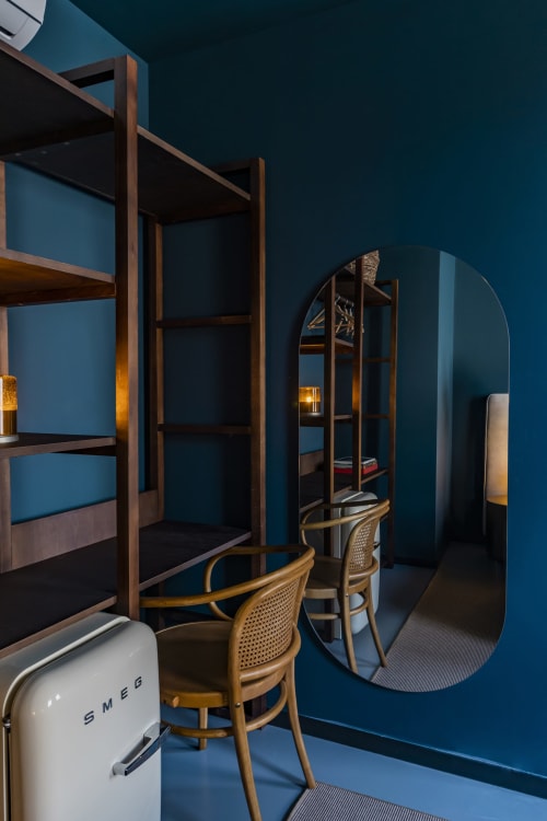 Estudio moderno en hotel Porto con paredes azul verdoso, estantes de madera, sillas de ratán, espejo redondo y refrigerador SMEG blanco