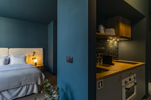 Modern studio apartment in Porto with blue-walled bedroom, kitchenette with wooden countertop, and ambient lighting