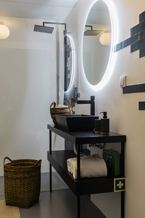 Modern black bathroom vanity with round LED mirror, black vessel sink, and woven baskets in Porto hotel studio
