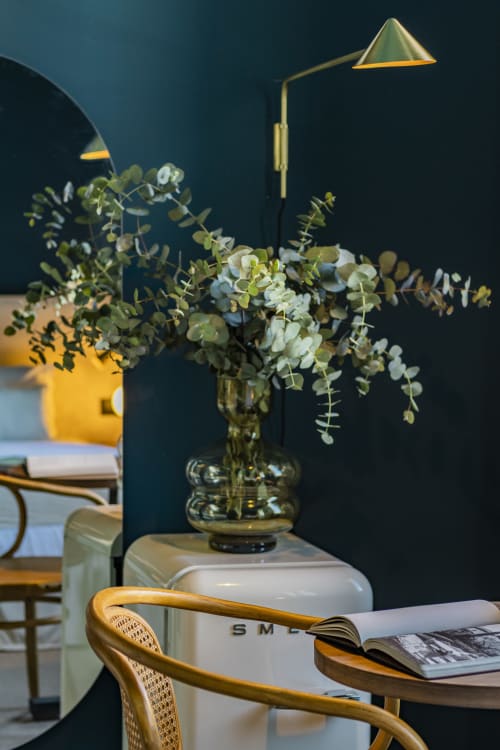 Compact studio in Porto hotel with eucalyptus arrangement in glass vase, brass desk lamp, and open magazine on wooden table