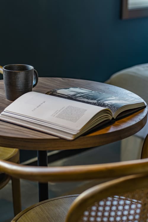 Libro abierto y taza de cerámica oscura sobre mesa de madera en estudio de hotel en Oporto con pared de color azul verdoso de fondo