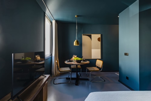 Estudio de hotel moderno en Oporto con paredes azul verdoso, mesa de comedor redonda, sillas de caña y lámpara colgante de latón