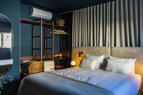 Dormitorio moderno de hotel en Porto con paredes turquesas, armario de madera, cama tapizada beige y cortinas rayadas.