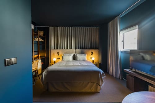 Moderno estudio en Oporto con paredes color verde azulado, iluminación dorada en cabecero y vistas a la ciudad en el hotel Benefit Collection