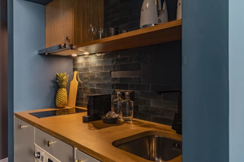 Kitchenette moderna en estudio de hotel en Oporto con armarios de madera, salpicadero de azulejos negros y fregadero de acero inoxidable
