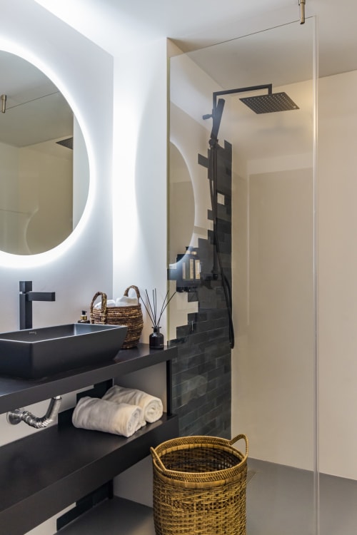Baño moderno del hotel Benefit Collection en Oporto con tocador negro, espejo iluminado, alcachofa de lluvia y tejido
