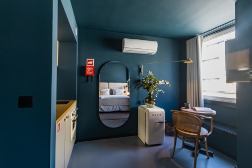 Estudio moderno y compacto en Oporto con paredes color turquesa, espejo ovalado, cocina americana, zona de trabajo y vistas de la ciudad