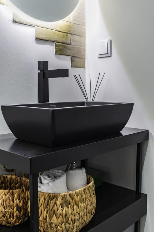 Lavabo negro moderno con grifo alto en el baño del hotel Porto, espejo redondo y azulejos de pared metálicos