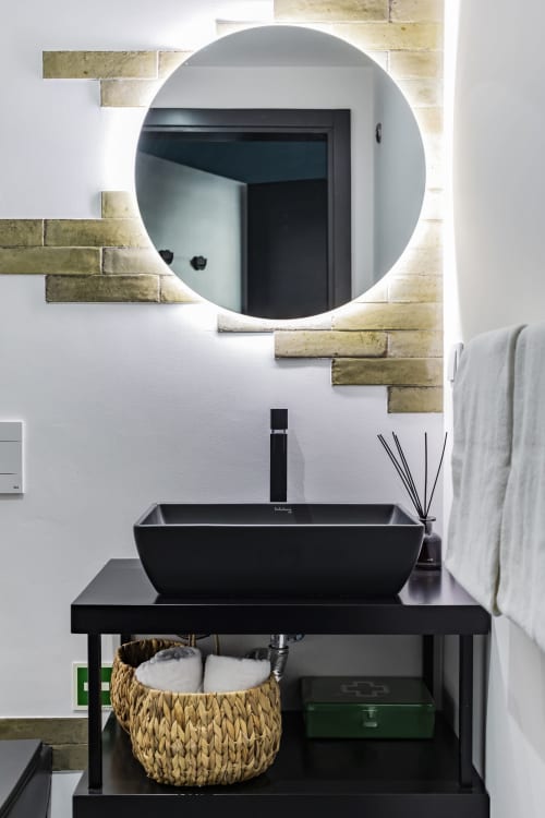 Baño moderno en hotel de Oporto con lavabo negro suspendido, espejo circular iluminado y detalles de ladrillos