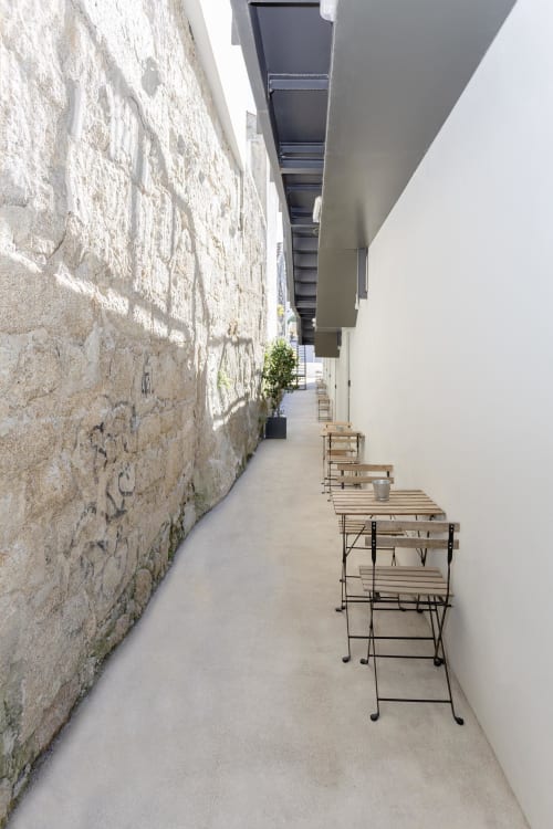 Narrow courtyard at Benefit Collection hotel in Porto with rustic stone wall and modern wooden tables