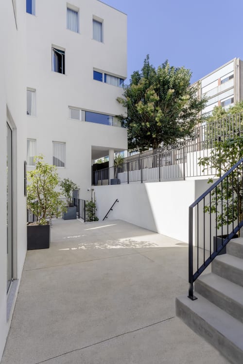 Modern hotel courtyard in Porto with white building, contemporary stairs, black railings, and green landscaping under clear