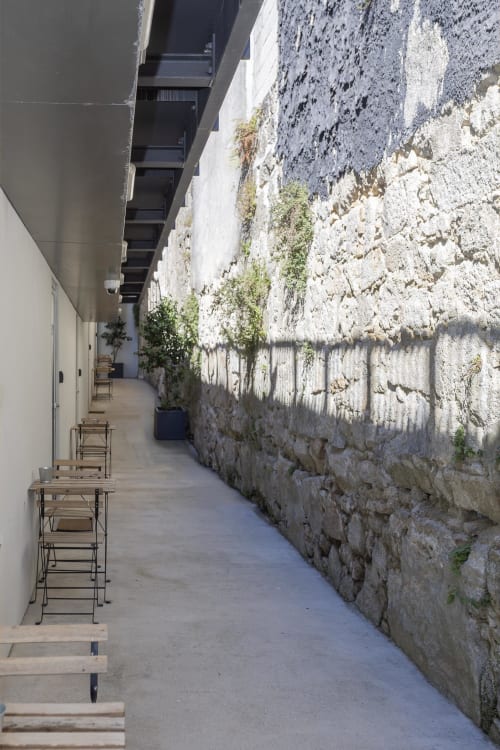 Narrow alleyway at Benefit Collection hotel Porto, featuring stone walls with vegetation and modern seating.