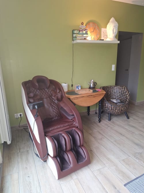 Espace bien-être moderne à La Cour d'Hortense B&B avec fauteuil de massage bordeaux, mobilier en rotin rond et table en bois