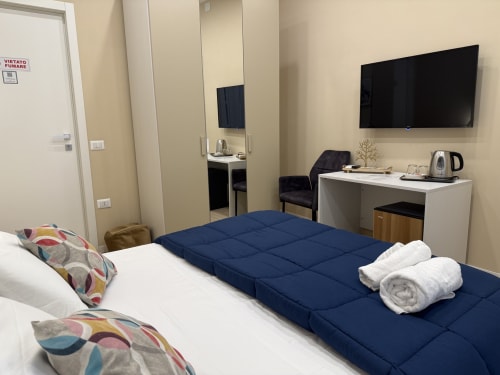 Camera moderna dell'Encanto Naples con letto matrimoniale, coperta blu, TV a schermo piatto, scrivania e vista sulla città