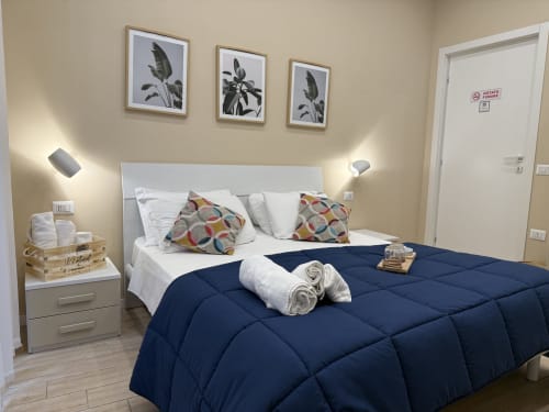 Camera moderna dell'Hotel Encanto Naples con piumone blu navy, biancheria bianca, cuscini colorati, arte botanica a parete e illuminazione ambient